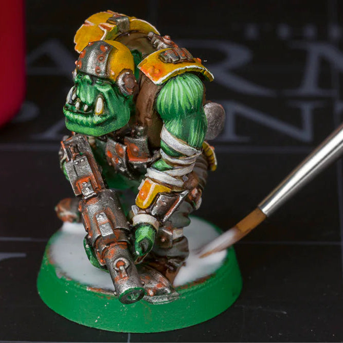 Miniature figure being painted with a brush on a black surface with 'Warren's Wargaming Tools' branding.